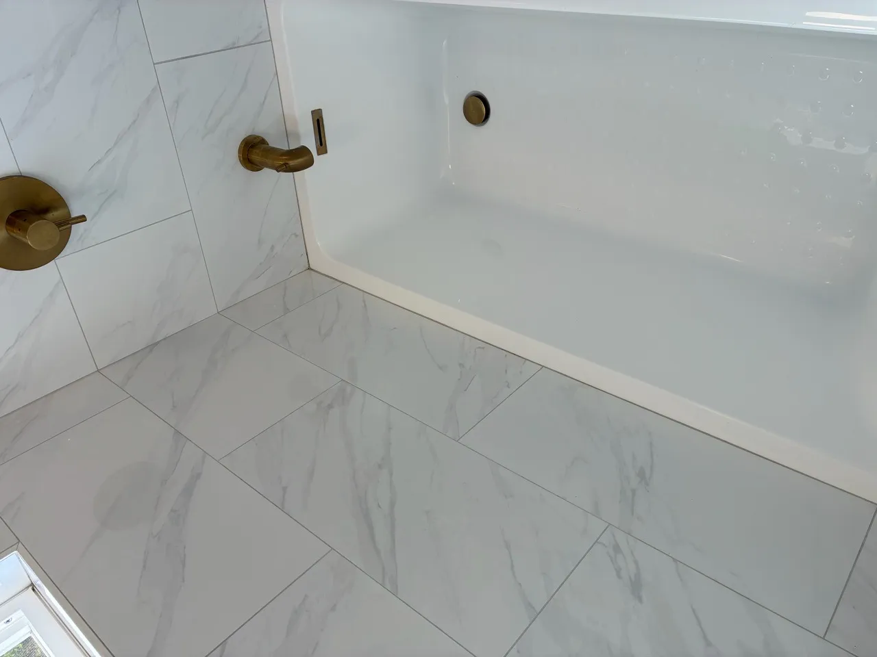 White bathtub surrounded by marble-look tile and brass fixtures
